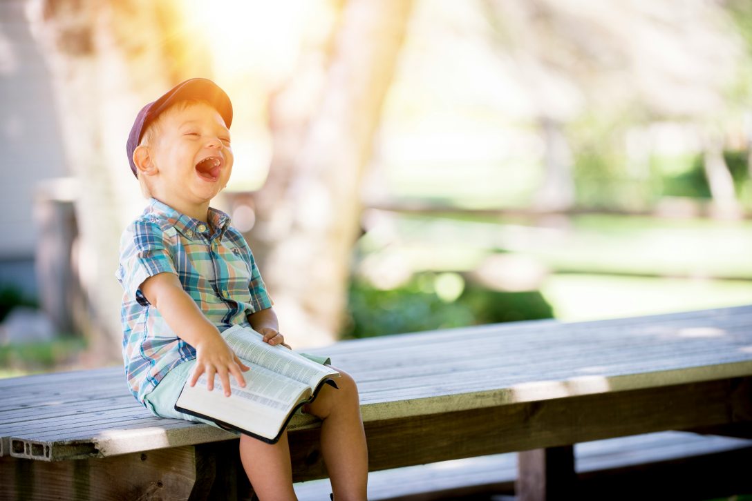 Little boy laughing on bench with Bible